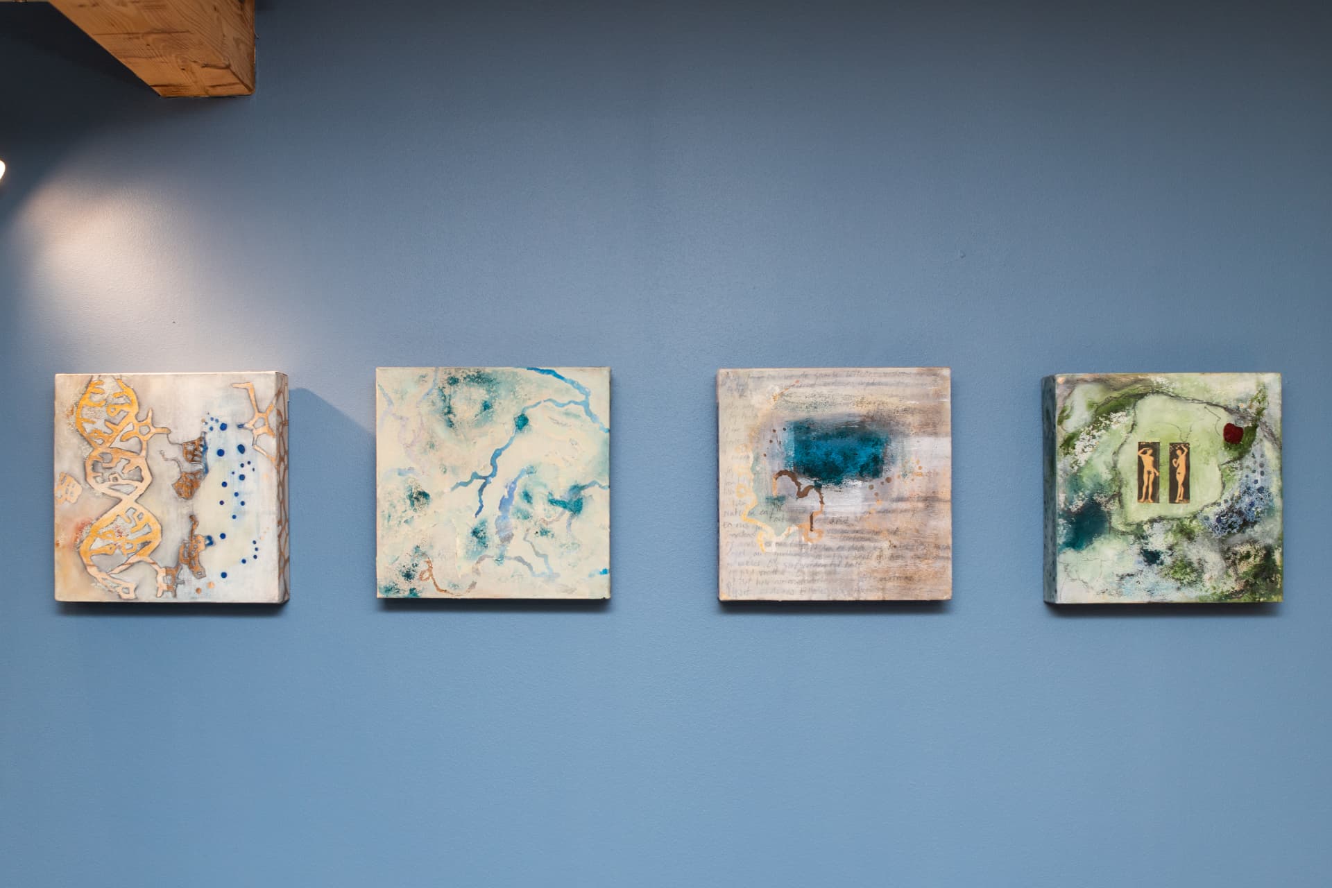 Four paintings from the Origins of Life series hanging in a row on a blue wall