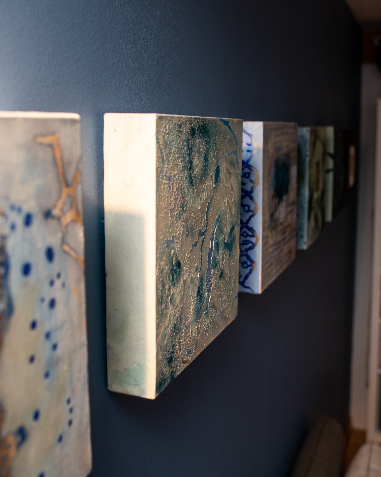 Side view of the Origins of Life series canvases on a blue wall