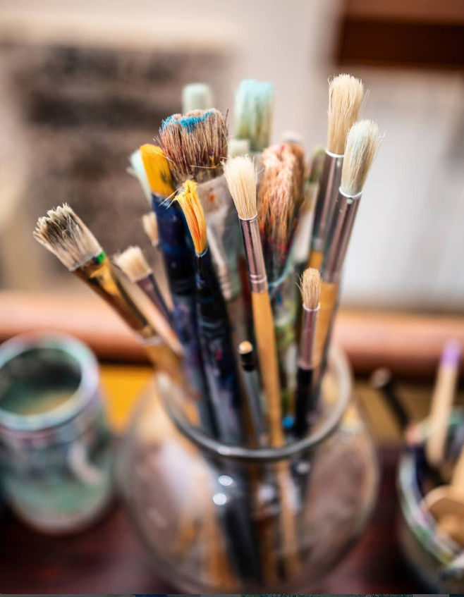 Used paintbrushes with yellow, turquoise and blue-tipped bristles standing in a glass jar