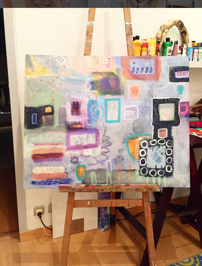 A finished abstract painting in pastel purples, pinks, teals and oranges with bold black-and-white shapes, resting on a wooden easel